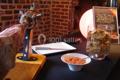 Jambon sur support, bol de tartare et croûtons disposés sur une table devant un mur en briques.