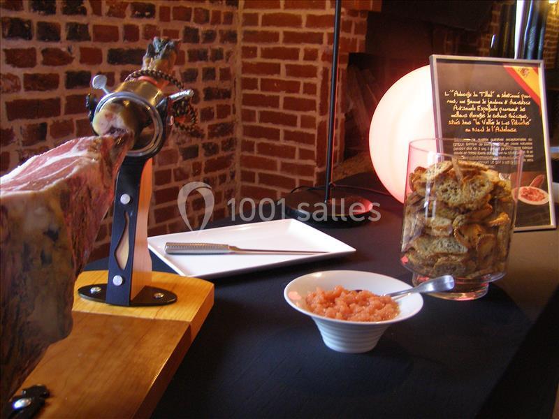 Jambon sur support, bol de tartare et croûtons disposés sur une table devant un mur en briques.