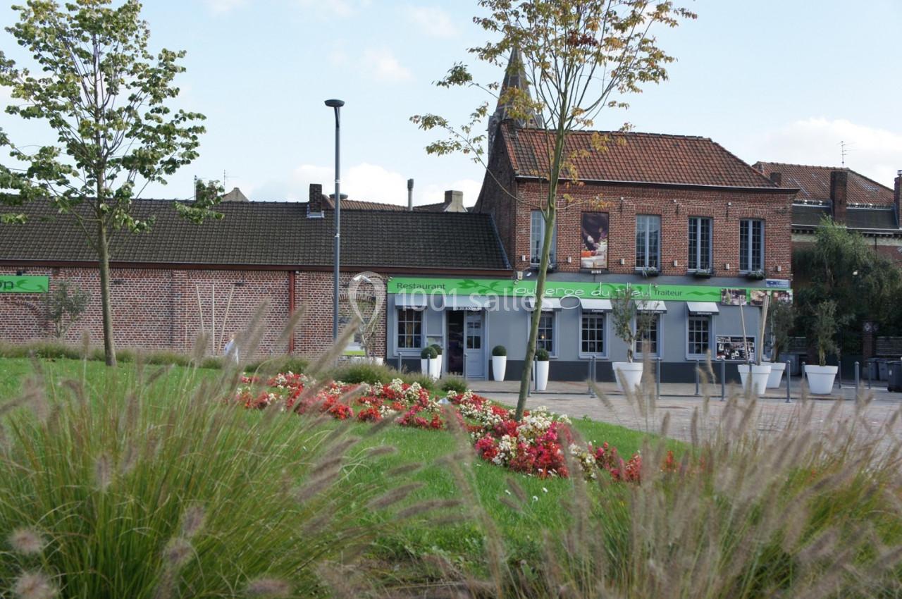 Façade d'un restaurant en briques rouges avec terrasse, entouré de parterres fleuris et d'arbres.