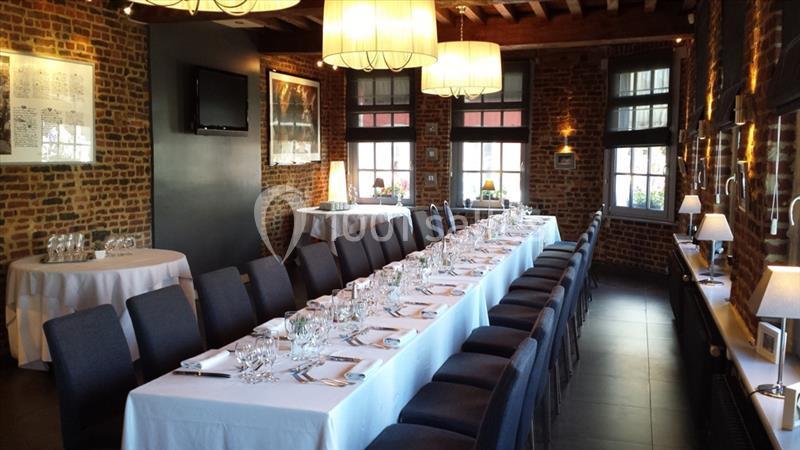 Salle à manger avec une longue table dressée, entourée de chaises, dans un décor en briques apparentes.