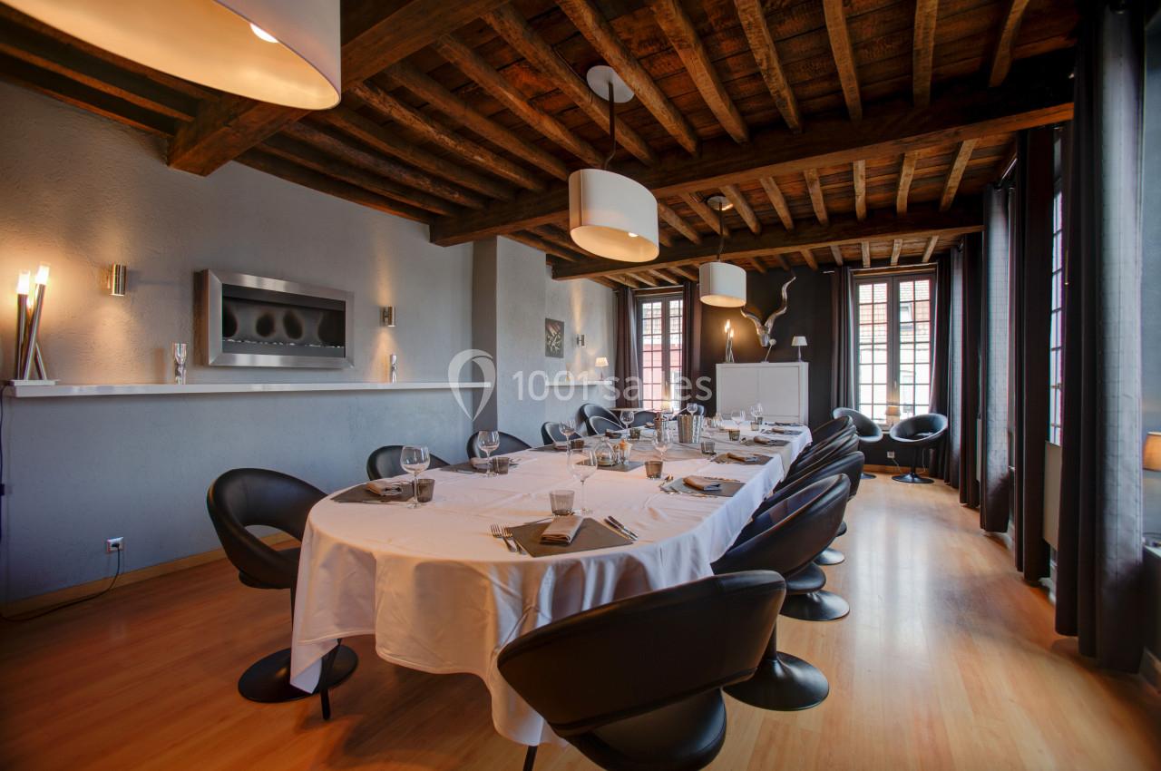 Salle à manger élégante avec grande table dressée, chaises noires, plafond en bois et lumière naturelle.