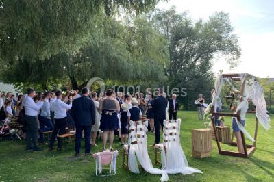 Miniature Location salle Paillencourt (Nord) - Le Canotier #7 Table en bois décorée de bougies, fleurs et feuillage, entourée de chaises, sous une arche végétale dans une salle lumineuse.