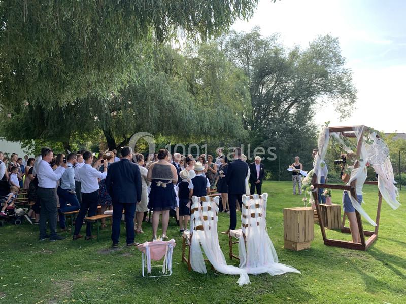 Cérémonie de mariage en plein air avec des invités rassemblés autour d'une arche décorée, sous des arbres.