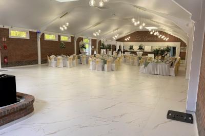 Miniature Location salle Paillencourt (Nord) - Le Canotier #4 Table en bois décorée de bougies, fleurs et feuillage, entourée de chaises, sous une arche végétale dans une salle lumineuse.