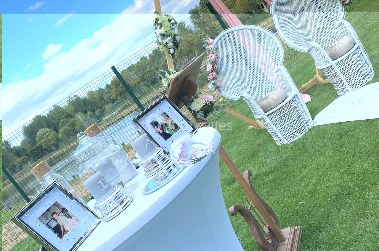 Décoration de mariage en extérieur avec chaises blanches, arche fleurie et table ornée de cadres photo et accessoires.