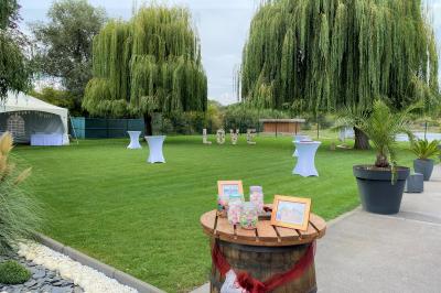 Miniature Location salle Paillencourt (Nord) - Le Canotier #6 Table en bois décorée de bougies, fleurs et feuillage, entourée de chaises, sous une arche végétale dans une salle lumineuse.
