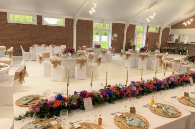 Miniature Location salle Paillencourt (Nord) - Le Canotier #10 Table en bois décorée de bougies, fleurs et feuillage, entourée de chaises, sous une arche végétale dans une salle lumineuse.
