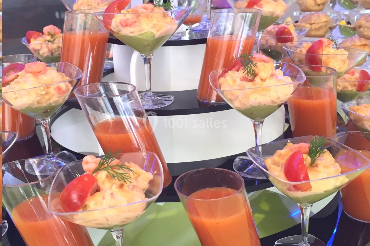 Présentoir avec verrines de soupe rouge, crevettes, avocat et tomates cerises, disposées sur plusieurs niveaux.