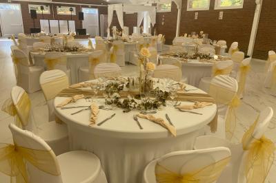 Miniature Location salle Paillencourt (Nord) - Le Canotier #12 Table en bois décorée de bougies, fleurs et feuillage, entourée de chaises, sous une arche végétale dans une salle lumineuse.