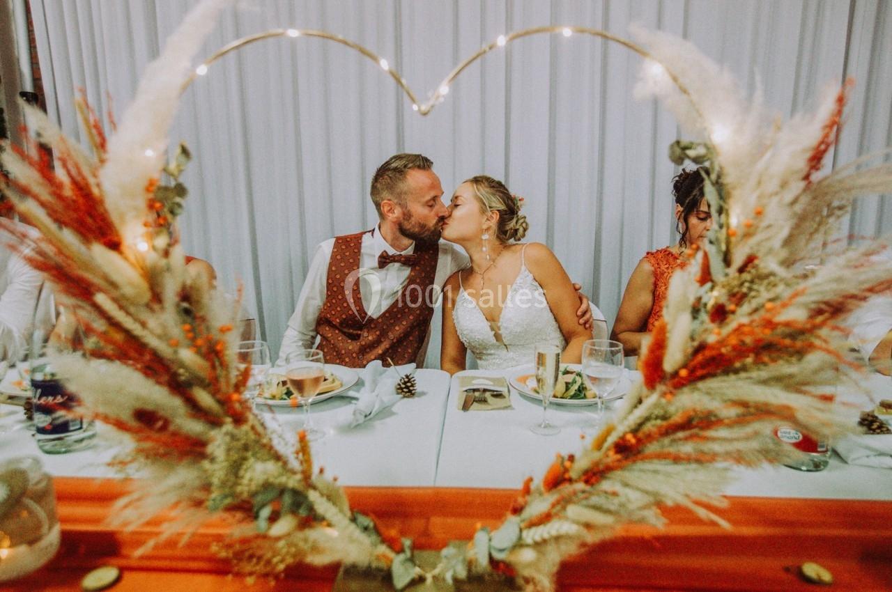 Un couple s'embrasse tendrement lors d'un repas de mariage, encadré par une décoration en forme de cœur.