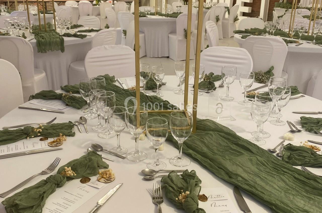 Salle de réception décorée avec des tables rondes, nappes blanches, centres de table fleuris et chemins de table verts.