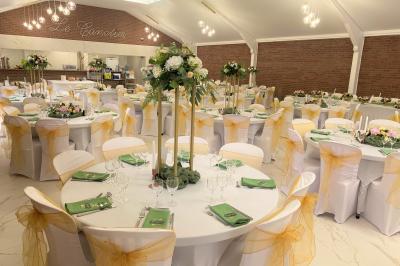 Miniature Location salle Paillencourt (Nord) - Le Canotier #23 Table en bois décorée de bougies, fleurs et feuillage, entourée de chaises, sous une arche végétale dans une salle lumineuse.