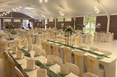 Miniature Location salle Paillencourt (Nord) - Le Canotier #24 Table en bois décorée de bougies, fleurs et feuillage, entourée de chaises, sous une arche végétale dans une salle lumineuse.