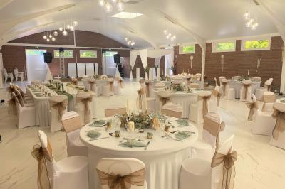 Miniature Location salle Paillencourt (Nord) - Le Canotier #26 Table en bois décorée de bougies, fleurs et feuillage, entourée de chaises, sous une arche végétale dans une salle lumineuse.