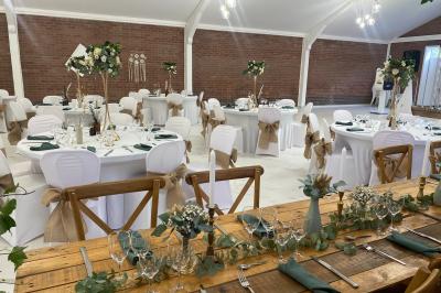 Miniature Location salle Paillencourt (Nord) - Le Canotier #27 Table en bois décorée de bougies, fleurs et feuillage, entourée de chaises, sous une arche végétale dans une salle lumineuse.