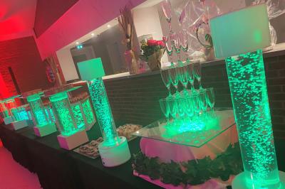 Miniature Location salle Paillencourt (Nord) - Le Canotier #30 Table en bois décorée de bougies, fleurs et feuillage, entourée de chaises, sous une arche végétale dans une salle lumineuse.