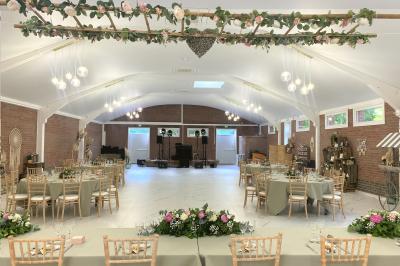 Miniature Location salle Paillencourt (Nord) - Le Canotier #35 Table en bois décorée de bougies, fleurs et feuillage, entourée de chaises, sous une arche végétale dans une salle lumineuse.