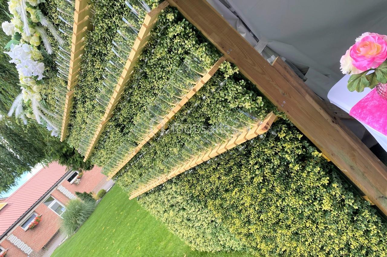 Mur végétal incliné avec des plantes et des rangées de vases en verre, installé dans un jardin extérieur.