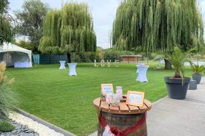 Miniature Location salle Paillencourt (Nord) - Le Canotier #40 Table en bois décorée de bougies, fleurs et feuillage, entourée de chaises, sous une arche végétale dans une salle lumineuse.