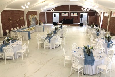 Salle de réception décorée avec des tables rondes blanches, nappes élégantes et chaises assorties, prête pour un événement.