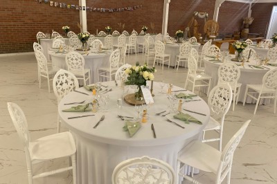 Salle de réception décorée avec des tables rondes blanches, nappes élégantes et chaises assorties, prête pour un événement.