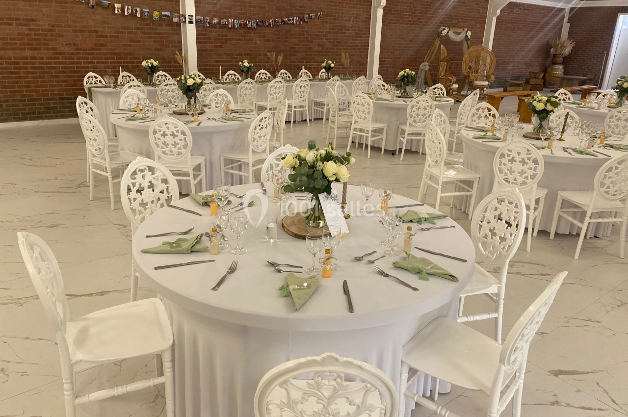 Salle de réception décorée avec des tables rondes dressées, nappes blanches, chaises assorties et centres de table fleuris.