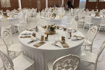 Salle de réception décorée avec des tables rondes blanches, nappes élégantes et chaises assorties, prête pour un événement.