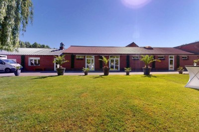 Tente blanche avec fenêtres en arc installée dans un jardin, entourée d'arbres et de pelouses sous un ciel dégagé.