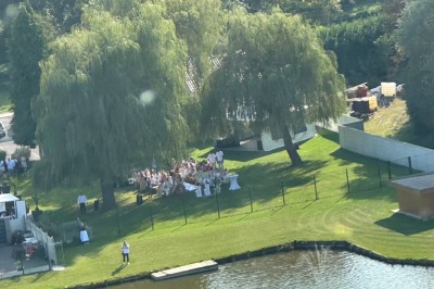 Tente blanche avec fenêtres en arc installée dans un jardin, entourée d'arbres et de pelouses sous un ciel dégagé.