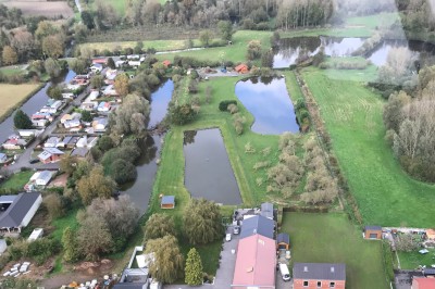 Tente blanche avec fenêtres en arc installée dans un jardin, entourée d'arbres et de pelouses sous un ciel dégagé.