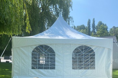 Tente blanche avec fenêtres en arc installée dans un jardin, entourée d'arbres et de pelouses sous un ciel dégagé.
