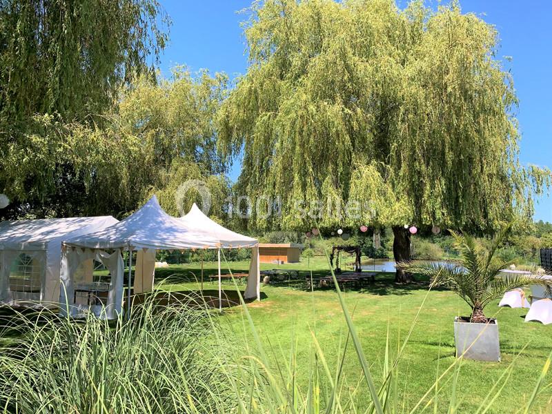 Tente blanche installée sur une pelouse verdoyante près d'un grand saule pleureur, sous un ciel bleu clair.