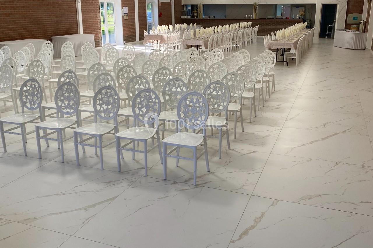 Salle de réception lumineuse avec des rangées de chaises blanches décoratives et un sol en carrelage effet marbre.
