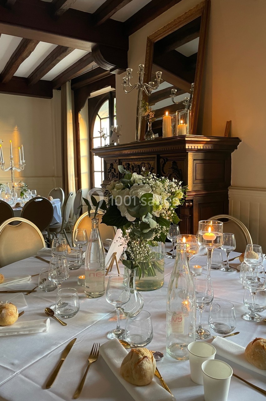 Table élégamment dressée avec des fleurs, bougies allumées et vaisselle raffinée dans une salle au décor classique.
