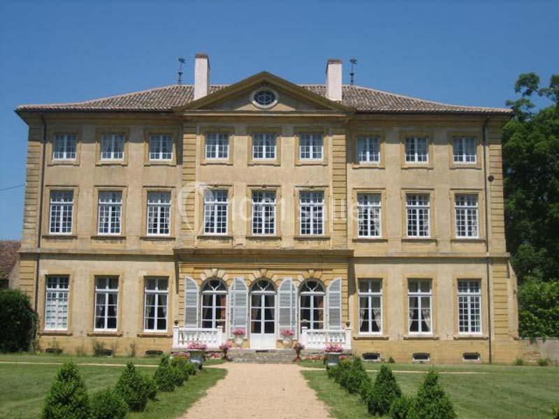 Façade d'un grand bâtiment ancien en pierre jaune avec des fenêtres symétriques, entouré de verdure.