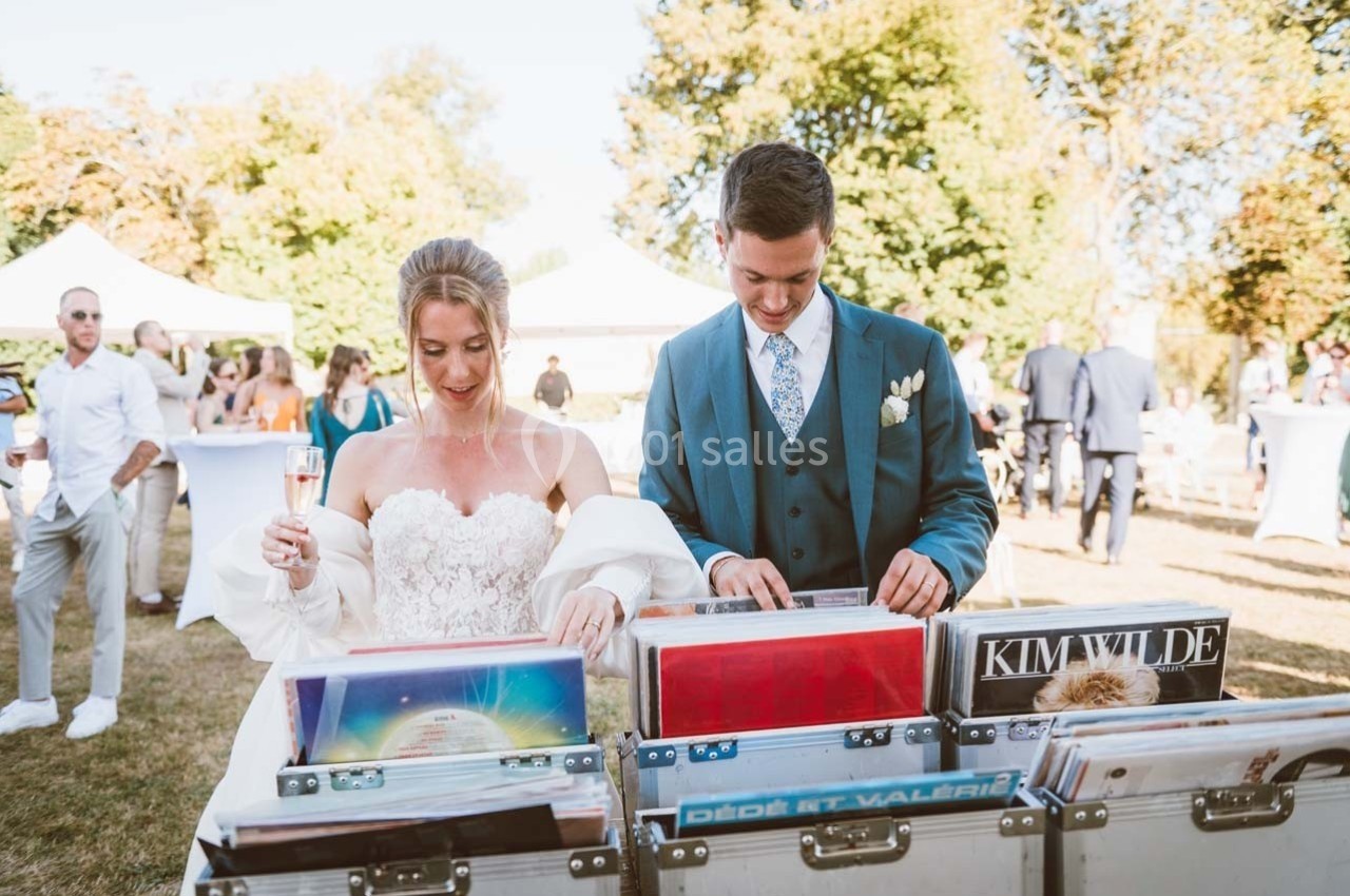 Un couple en tenue de mariage feuillette des vinyles lors d'une réception en plein air par une journée ensoleillée.