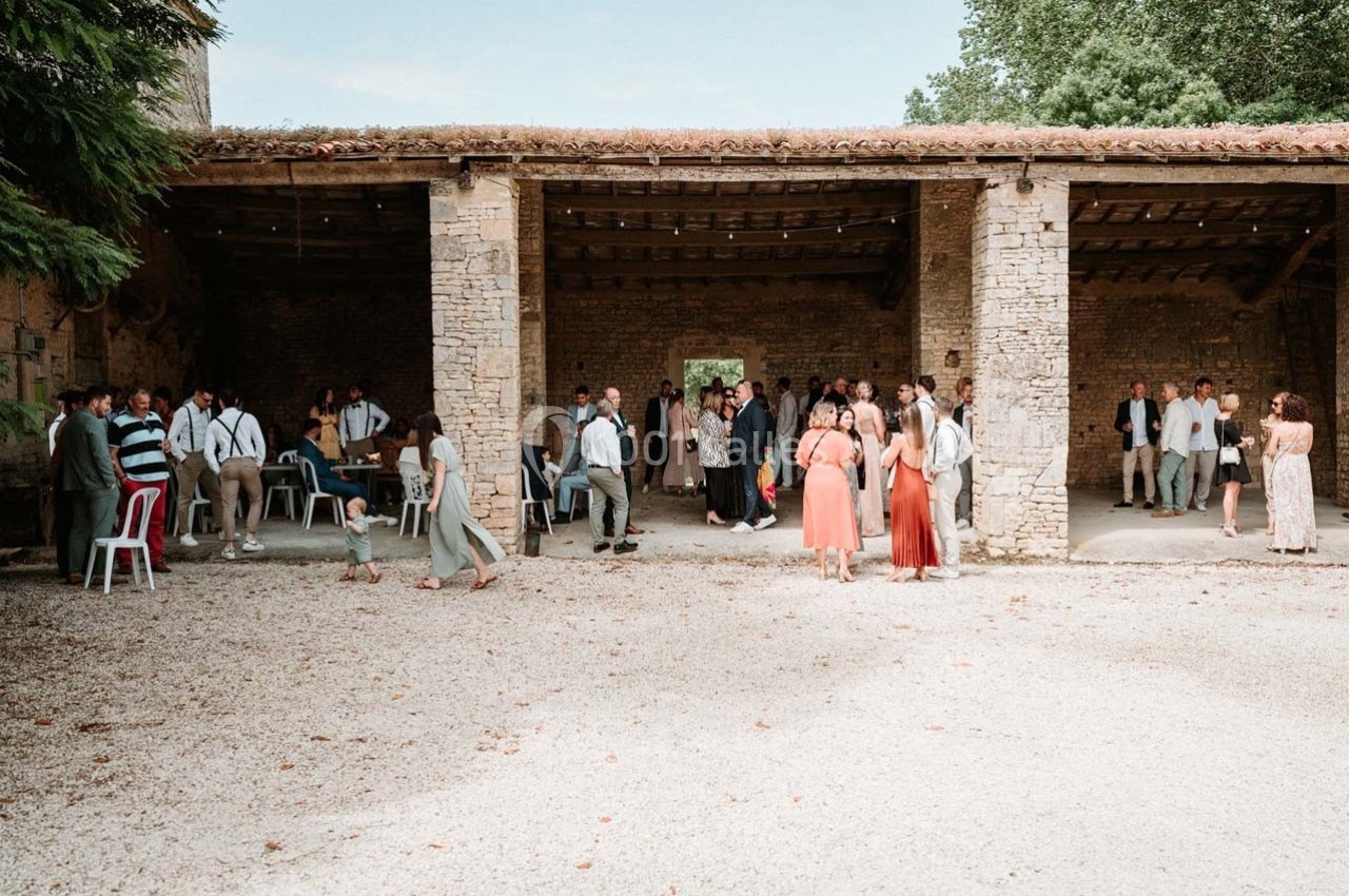 Groupe de personnes rassemblées dans une cour en pierre, sous un bâtiment ouvert, lors d'un événement en plein air.