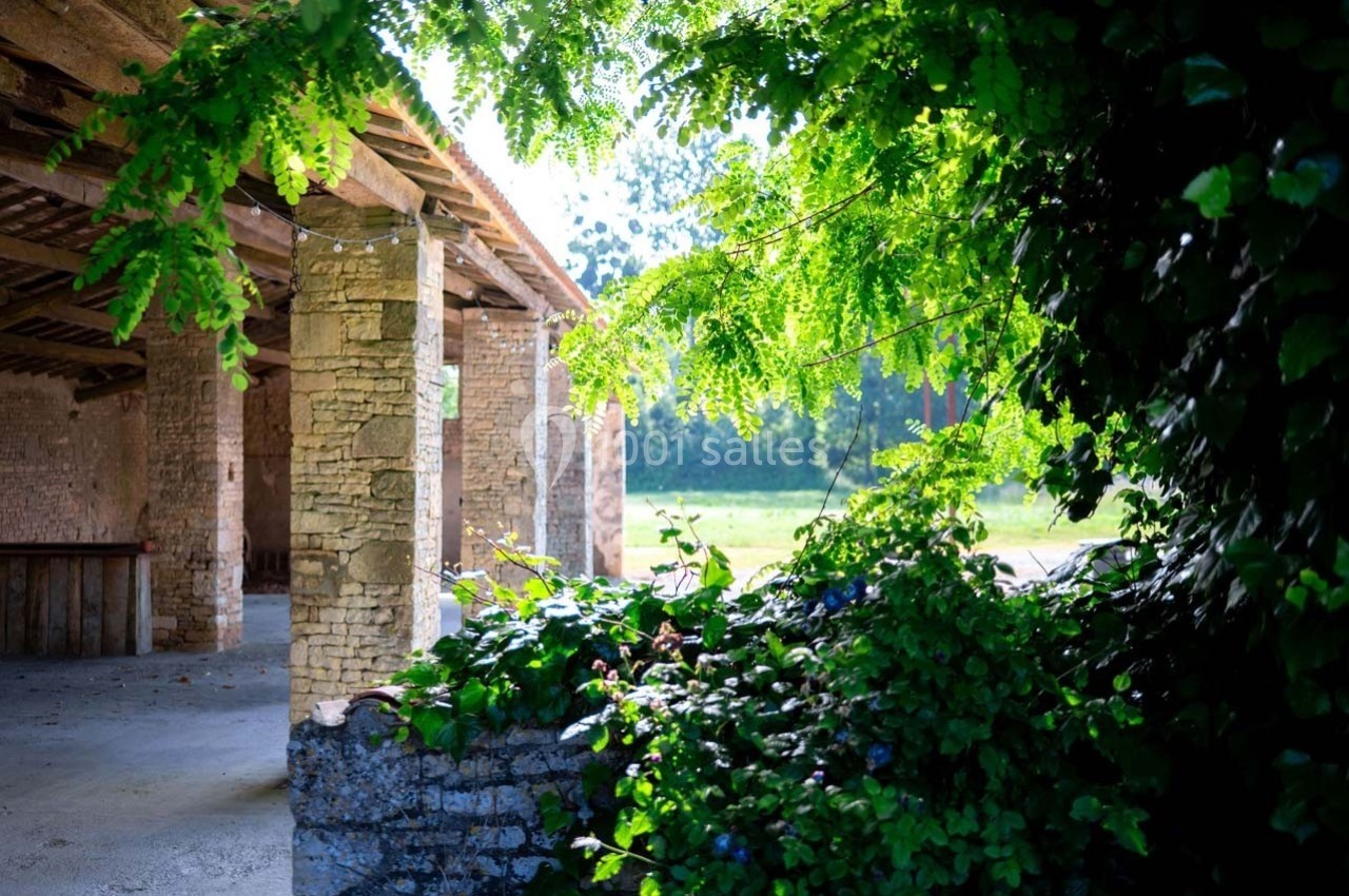 Vue d'un bâtiment en pierre ouvert sur un jardin verdoyant, entouré de feuillage et baigné de lumière naturelle.