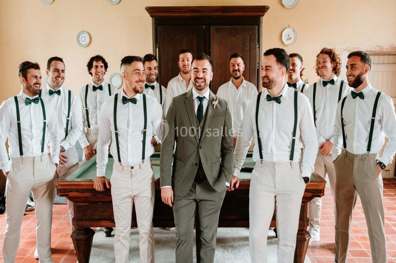 Un homme en costume entouré de plusieurs hommes en chemise blanche et bretelles, posant devant une table de billard.