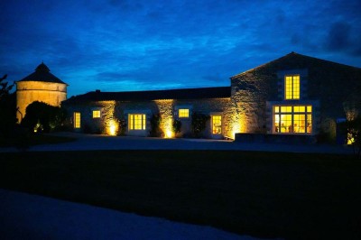 Bâtiment en pierre éclairé la nuit, avec un ciel bleu foncé en arrière-plan et un jardin sombre au premier plan.