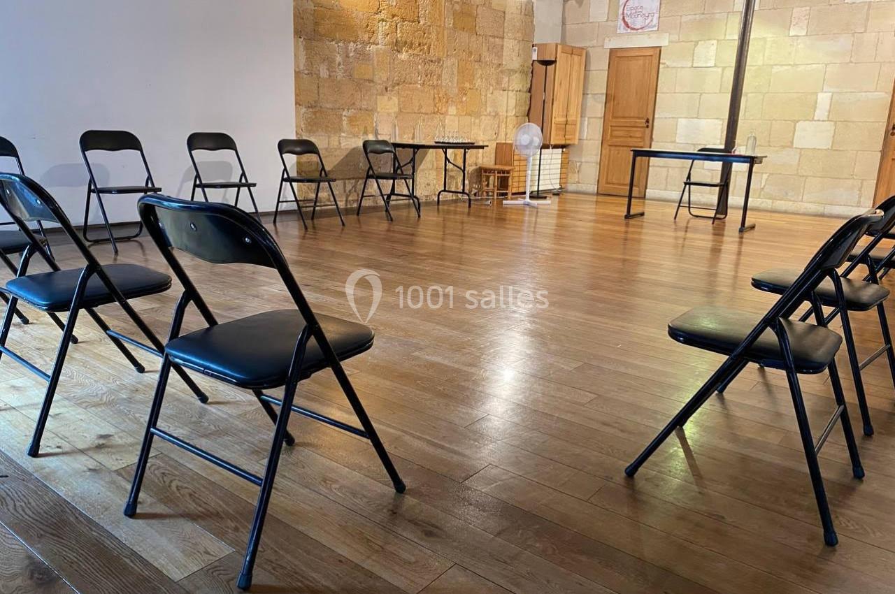 Chaises pliantes disposées en cercle dans une salle lumineuse avec parquet en bois et murs en pierre.