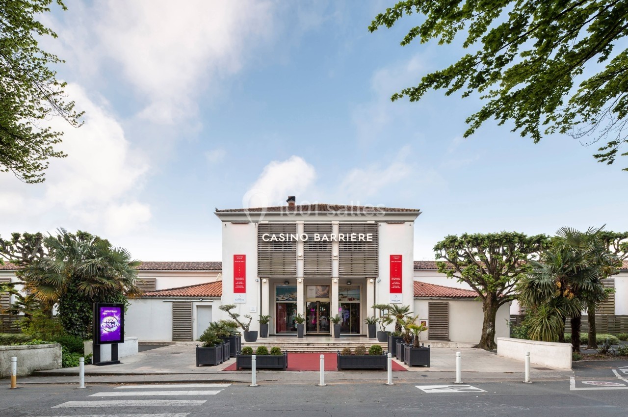 Façade d'un casino avec une entrée principale entourée de palmiers et un ciel dégagé en arrière-plan.