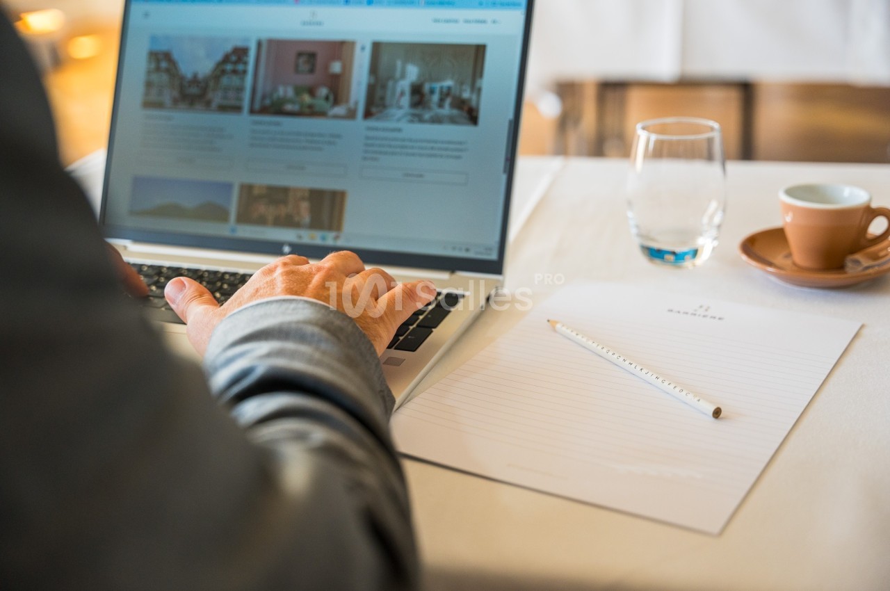 Une personne utilise un ordinateur portable sur une table avec un carnet, un crayon, un verre d'eau et une tasse de café.