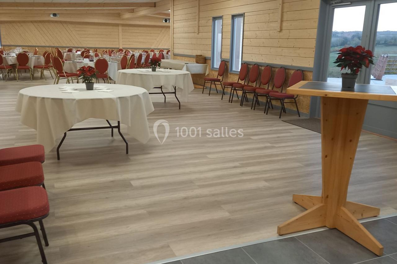 Salle de réception lumineuse avec tables rondes dressées, chaises rouges et décorations simples.