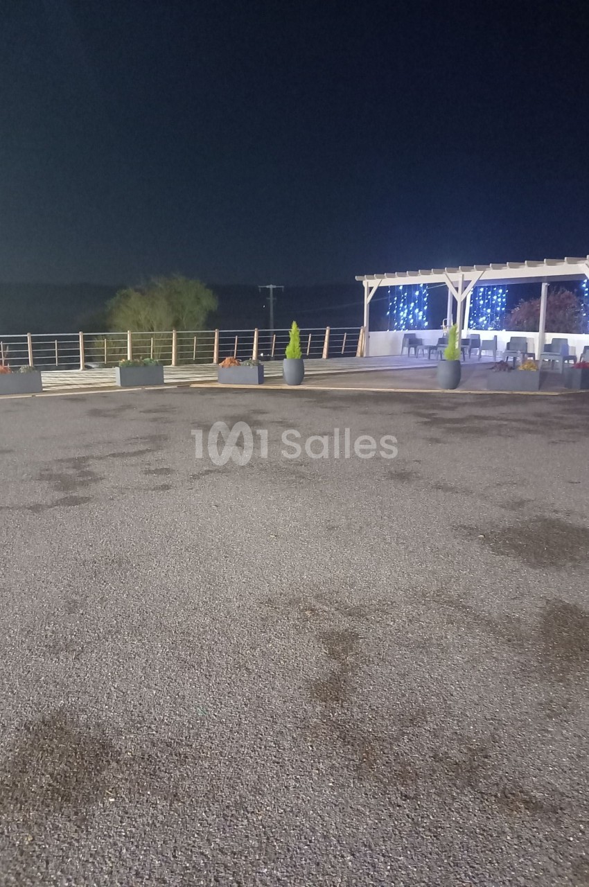 Espace extérieur de nuit avec pergola éclairée, pots de plantes et sol en gravier.