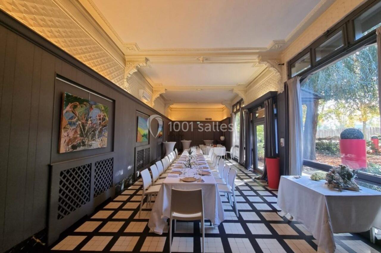 Salle lumineuse avec tables dressées en enfilade, grandes fenêtres donnant sur un espace extérieur arboré.