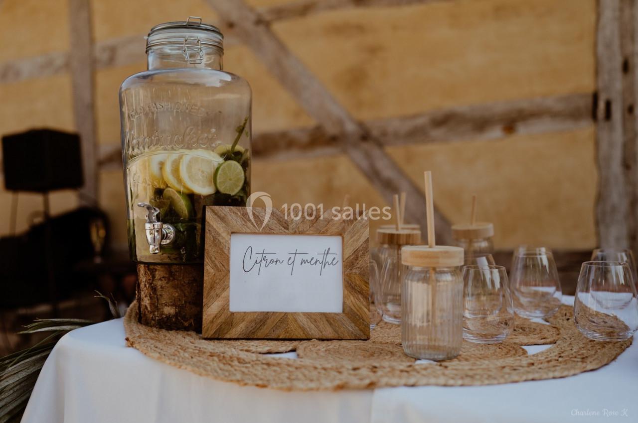 Distributeur de boisson citron et menthe avec verres en verre et pailles en bois sur une table décorée.