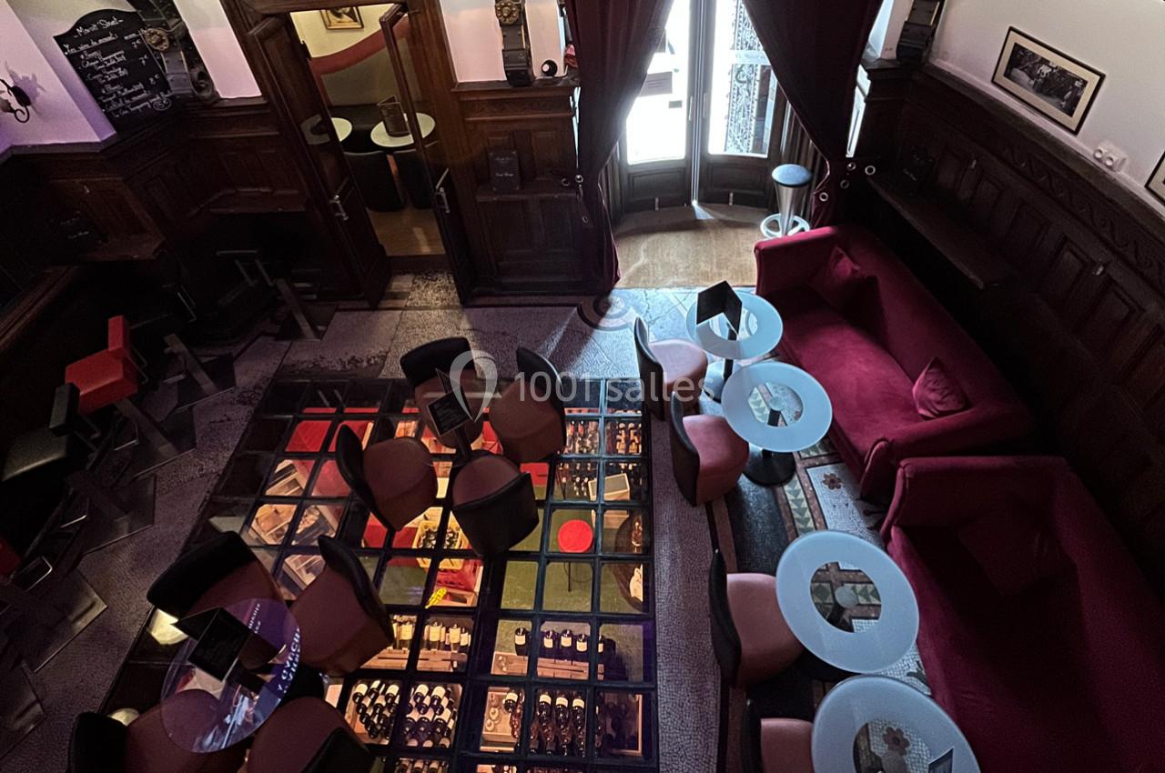 Salle de restaurant avec tables et fauteuils, sol en verre laissant voir une cave à vin éclairée en dessous.