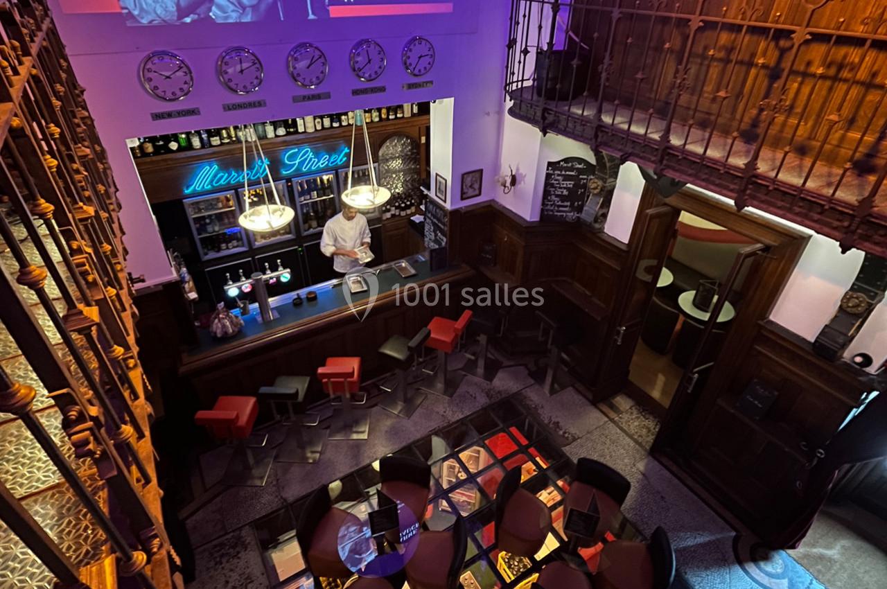 Vue plongeante d'un bar rétro avec un barman, des tables colorées et une ambiance chaleureuse.