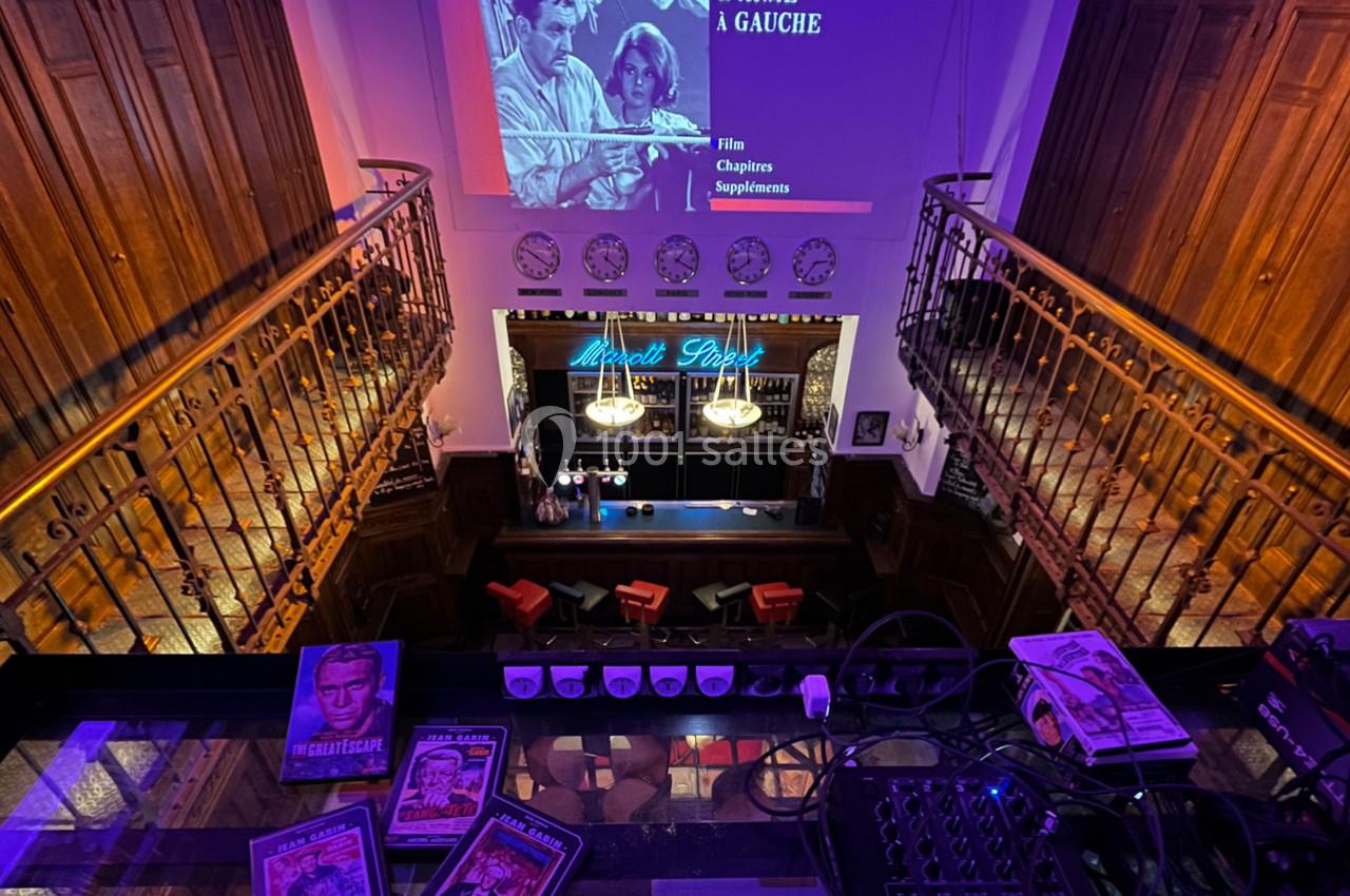 Vue d'un bar rétro avec un écran projetant un film, entouré de décorations vintage et de magazines anciens.